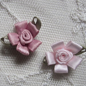 May include: Two small fabric rose embellishments, one in pink and one in a darker shade of pink. Both roses have a green leaf detail.