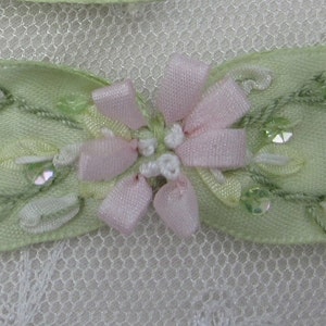 May include: A green satin ribbon bow with pink and white floral embellishments and sequins.