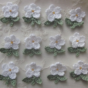 May include: Twelve white crocheted flowers with green leaves. Each flower has a yellow center.
