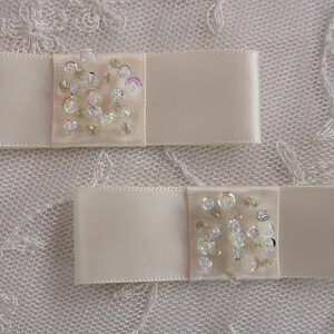 May include: Two ivory satin ribbon bows with a cluster of iridescent sequins in the centre of each bow.