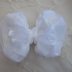May include: A white, layered, fabric bow with a ruffled texture.