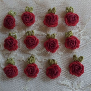 May include: Twelve red fabric rose embellishments with green leaves. The roses are sewn together in a circular shape and have a textured appearance.