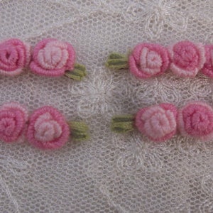 May include: Four sets of three pink felt roses with green felt leaves. The roses are arranged in a row and are attached to a white background.