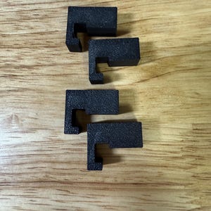 May include: Four black plastic corner brackets with a small lip on the top edge. The brackets are arranged in a vertical stack.