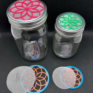 May include: Two glass jars with lids featuring a geometric flower design. The lids are red and green. Two additional lids are shown, one with a blue rim and the other with a white mesh.