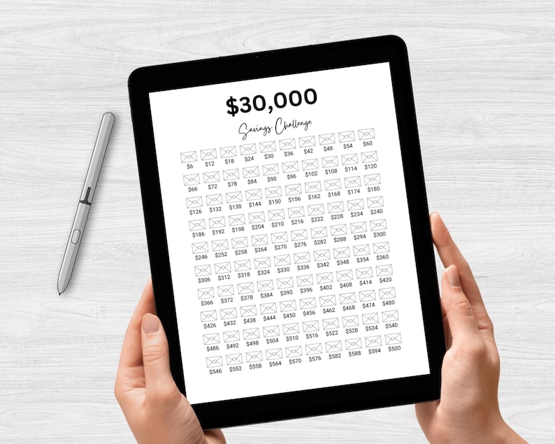May include: A black and white digital tablet displaying a savings challenge tracker with a grid of 100 envelopes. Each envelope has a dollar amount printed on it, starting at $6 and increasing by $2 up to $500. The text "$30,000 Savings Challenge" is at the top of the tablet.