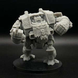 May include: A gray miniature war machine model with a detailed design. The model is posed on a black circular base, with its fists clenched. The model has intricate details, including panels, rivets, and symbols.
