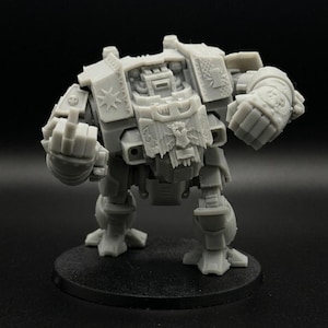 Puede incluir: Modelo gris en miniatura de máquina de guerra con un diseño detallado. El modelo está sobre una base circular negra. El robot tiene dos puños y está listo para la batalla. El modelo es de plástico.