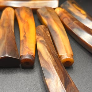 Op de afbeelding: Een verzameling vintage Bakeliet handgrepen in amberkleuren met een gemarmerd patroon. De handgrepen hebben een rechthoekige vorm met afgeronde of facet geslepen uiteinden. De kleuren variëren van lichtoranje tot donkerbruin.