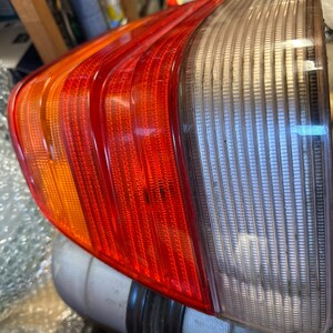 Op de afbeelding: Een achterlicht van een auto met rode, oranje en heldere secties. De rode sectie is het grootst, met een reeks parallelle lijnen. De heldere sectie heeft verticale lijnen. Het licht is schuin.