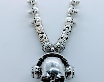 May include: Silver necklace with a skull pendant wearing headphones. The necklace is made of small skull beads.