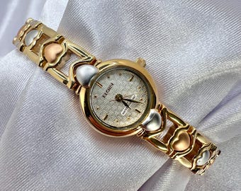 Reloj vintage nuevo de stock antiguo para mujer Elgin en tono dorado con correa en forma de corazón en dos tonos, elegante, delicado y con clase