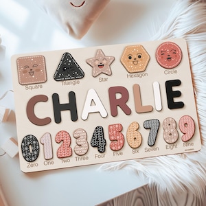 May include: A wooden educational puzzle board featuring the name CHARLIE in large letters, with cutouts for shapes labeled Square, Triangle, Star, Hexagon, Circle, and numbers zero through nine, each decorated with various patterns and colors.