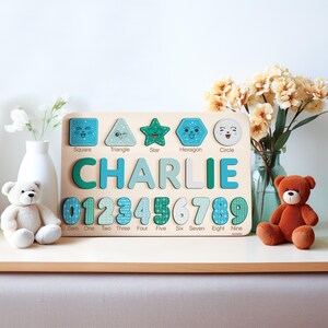 May include: A wooden educational toy with a blue and green colour scheme. The toy features a personalised name "CHARLIE" and includes shapes, numbers, and their corresponding names.