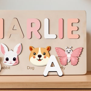 Peut inclure: Un puzzle en bois avec le nom "CHARLIE" &eacute;crit en lettres roses et blanches. Le puzzle comprend &eacute;galement des images d'un lapin, d'un chien et d'un papillon, avec les mots "lapin", "chien" et "mouche" &eacute;crits sous chaque image.