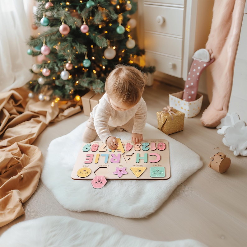 May include: A wooden puzzle with the name "CHARLIE" and numbers 0-9 in pastel colors. The puzzle includes various shapes with faces. A baby is playing with the puzzle on a white rug near a Christmas tree.