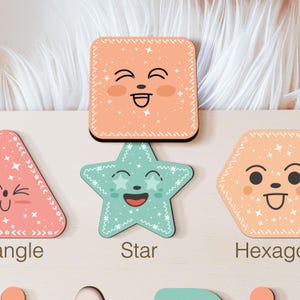 May include: A wooden educational toy featuring various shapes, each with a smiling face. The shapes include a triangle, square, star, and hexagon. The shapes are labelled with their names.