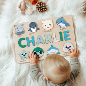 Peut inclure: Un puzzle en bois avec des illustrations d'animaux color&eacute;s et le nom "CHARLIE" &eacute;crit en grandes lettres color&eacute;es. Le puzzle est con&ccedil;u pour les enfants et pr&eacute;sente une vari&eacute;t&eacute; de cr&eacute;atures marines, notamment un hippopotame, une orque, un ours polaire, un dauphin, une &eacute;toile de mer, une tortue, un requin et un phoque moine.
