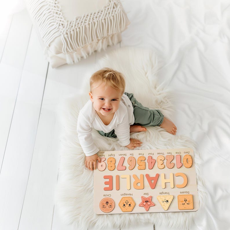 May include: A wooden puzzle with colourful numbers, shapes, and the name "CHARLIE" on a white background. A young child is playing with the puzzle.