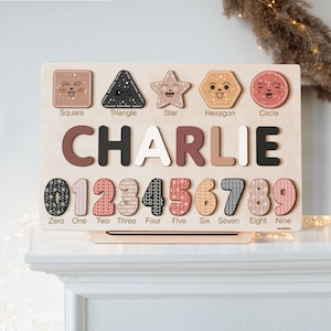 May include: Wooden educational toy with a personalised name "CHARLIE" in colourful letters. The toy features a puzzle with shapes, numbers, and their corresponding names. The shapes include a square, triangle, star, hexagon, and circle. The numbers are 0 through 9.