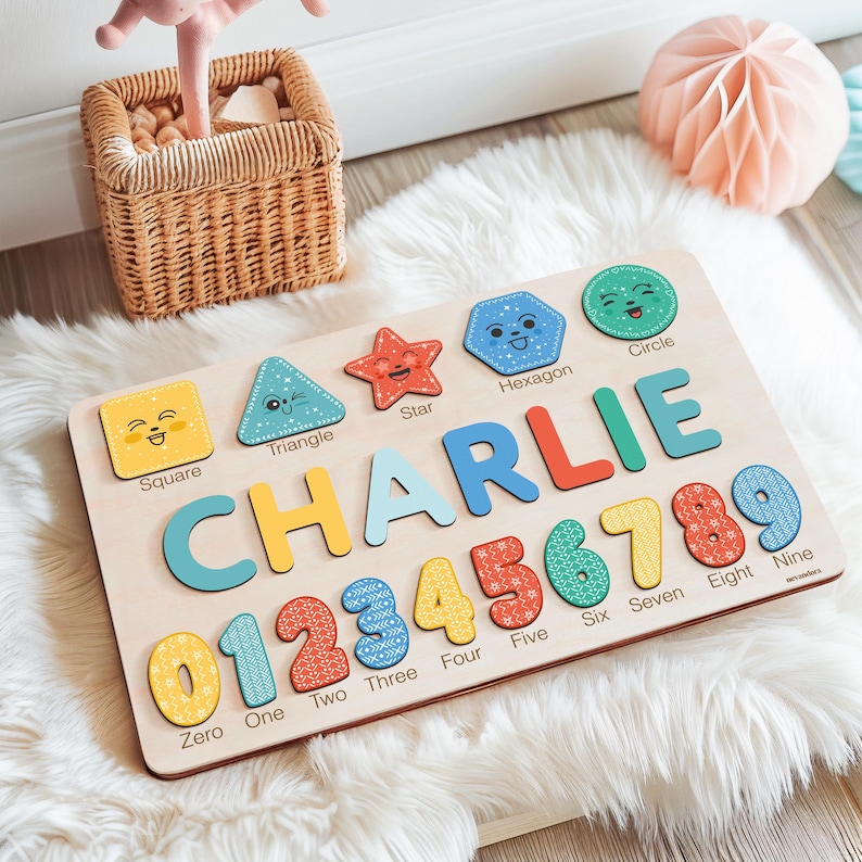 May include: A wooden puzzle board with colourful shapes, numbers, and letters. The board features a square, triangle, star, hexagon, and circle with happy faces. The name "CHARLIE" is spelled out in large letters, and the numbers 0 through 9 are displayed below.