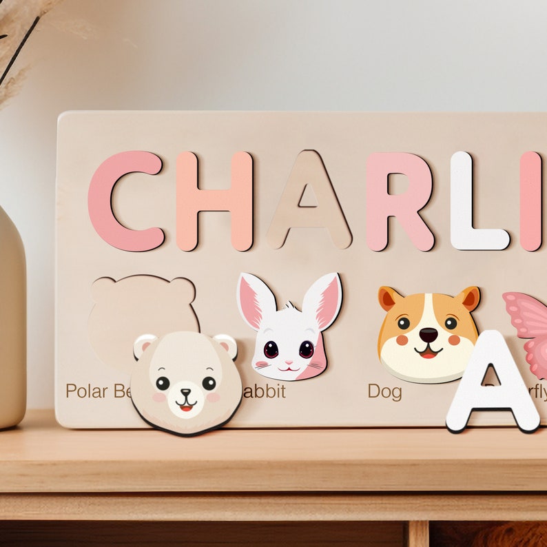 Peut inclure: Un puzzle en bois avec le nom CHARLIE &eacute;crit en lettres roses et blanches. Le puzzle pr&eacute;sente &eacute;galement des illustrations d'animaux : un ours polaire, un lapin, un chien et un papillon.