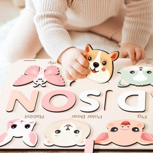 May include: A wooden puzzle with colorful animal and letter pieces. The puzzle features the letters D, I, S, O, and N. The animal pieces include a butterfly, a pig, a polar bear, a rabbit, and a dog. The puzzle is designed for children to learn the alphabet and animal names.