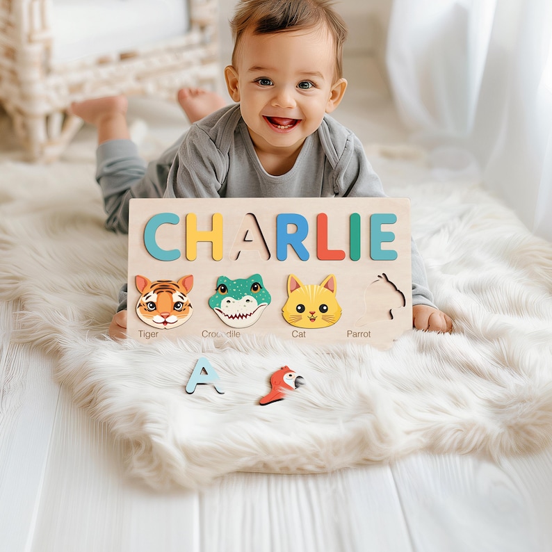 May include: A wooden personalized puzzle board with the name "CHARLIE" spelled out in colorful letters. The board features animal faces, including a tiger, crocodile, cat, and parrot, with corresponding labels below each animal. The puzzle pieces are missing from the board, and a few pieces are scattered on a white fluffy surface.