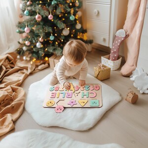 May include: A wooden puzzle with colourful letters spelling out the name "CHARLIE" and numbers 0-9. The puzzle also includes shapes with corresponding images of a bee, a hexagon, a star, a triangle, a square, and a circle. A young child is playing with the puzzle on a white fluffy rug.