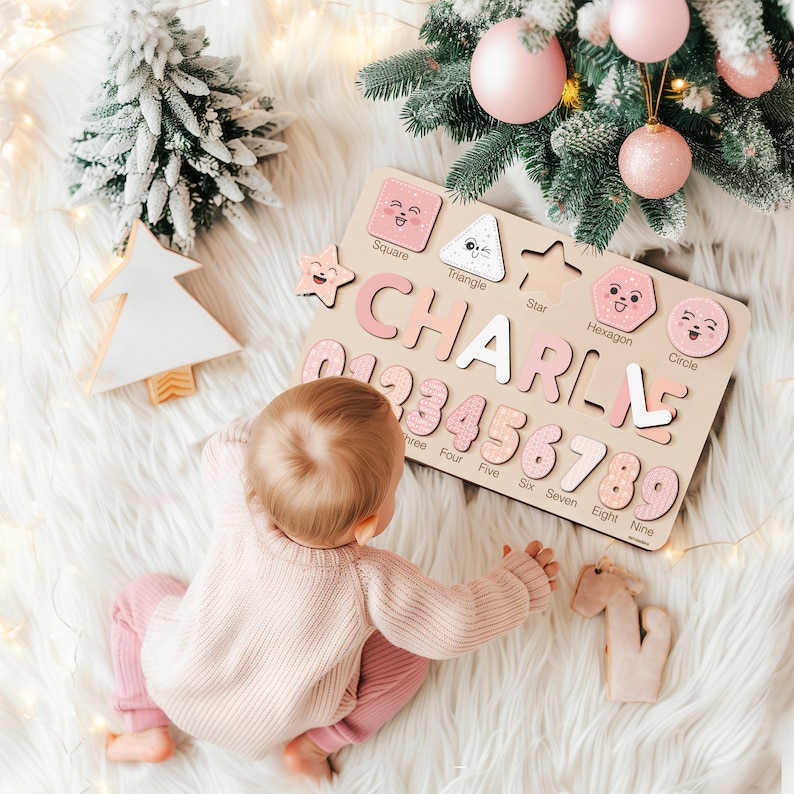 May include: A wooden puzzle board with pink and white pieces featuring the name "CHARLIE" and numbers 1 to 9. The board also includes shapes with faces, such as a square, triangle, star, hexagon, and circle. A baby is playing with the puzzle on a white fluffy surface.