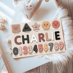 May include: A wooden puzzle with colorful shapes and numbers. The shapes include a square, triangle, star, hexagon, and circle. The numbers are 0 through 9. The name "CHARLIE" is spelled out in large letters on the puzzle.