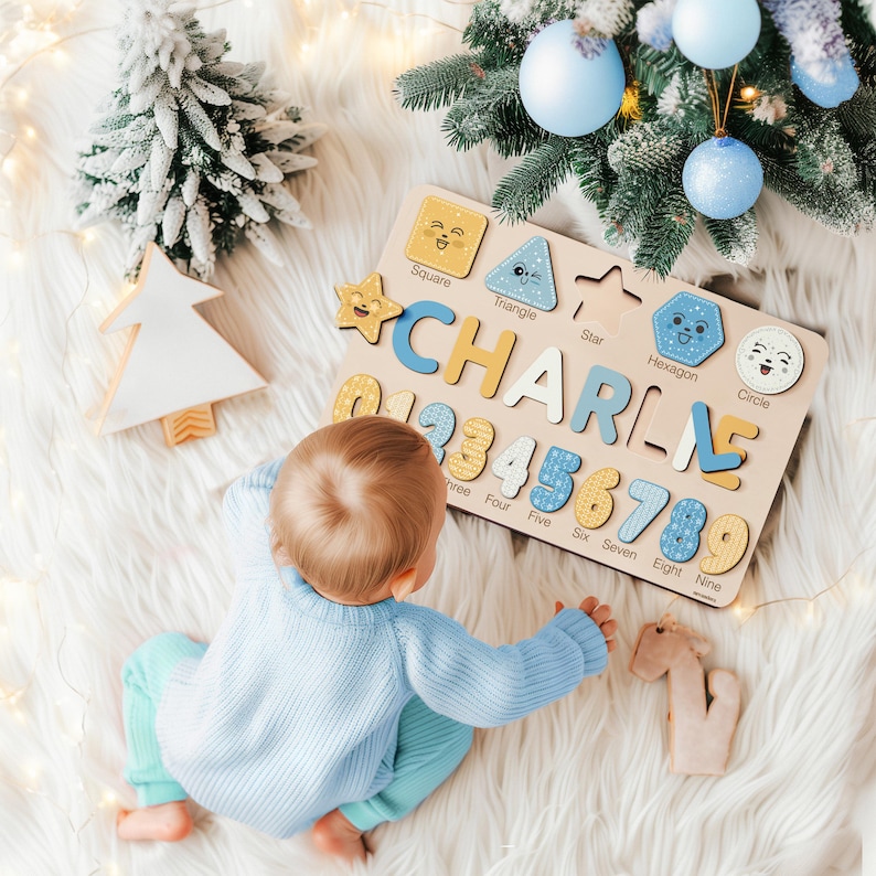 May include: Wooden puzzle board with the name "CHARLIE" spelled out in individual letters. The board also features numbers and shape cutouts. The puzzle is on a white fluffy surface, with a baby in a blue sweater and pants.