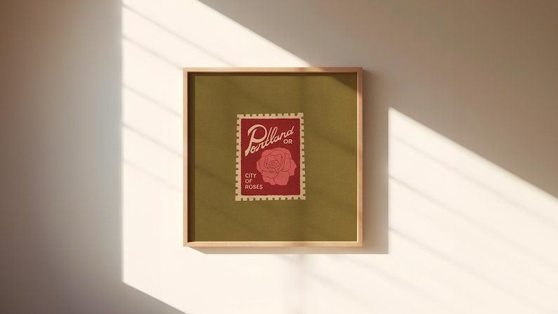 May include: Square framed art print featuring a vintage-style postage stamp design. The stamp, in red, displays the word "Portland OR" and a rose illustration, with "City of Roses" below. The background is olive green.