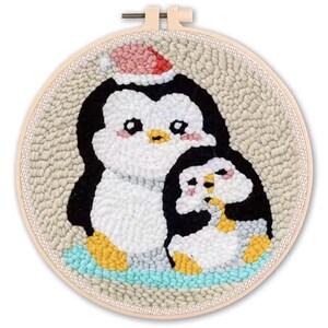 May include: A handmade, round embroidery hoop featuring two cartoon penguins. The larger penguin wears a red and white Santa hat. The penguins are black, white, and yellow, set against a beige background and a light blue base.