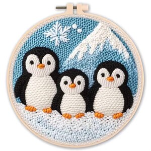 May include: A round, framed textile art piece featuring three penguins. The penguins have black and white bodies with orange beaks and feet, set against a blue background with a mountain and snowflake. The frame is a light beige color.