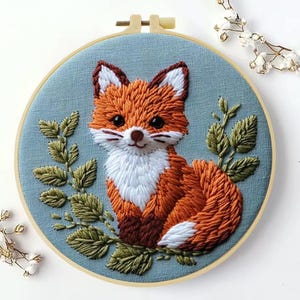 Könnte beinhalten: Gestickter Fuchs in einem Stickrahmen. Der Fuchs ist orange, weiß und braun, mit grünen Blättern auf hellblauem Hintergrund. Die Stickerei befindet sich in einem Holzreifen, ein charmantes, handgefertigtes Stück.