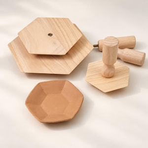 Può includere: Un set di componenti in legno chiaro che include due piattaforme esagonali a livelli con un foro centrale per vite in metallo, una base esagonale con manico verticale in legno e un piatto esagonale color terracotta.