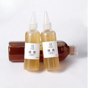 May include: Two clear plastic squeeze bottles filled with a light amber liquid, each featuring a white label with the Chinese characters 桃胶 and a smaller 100ml label. A third, larger dark amber bottle lies horizontally behind them.