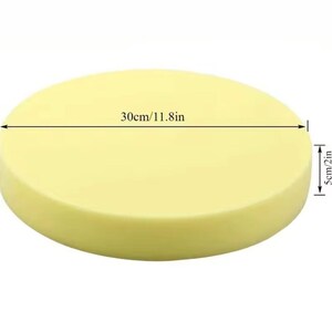 May include: A round, pale yellow object, 30cm (11.8in) in diameter and 5cm (2in) thick. The object has a smooth surface and a cylindrical shape. The image is taken from a slightly elevated angle, showing the entire object.
