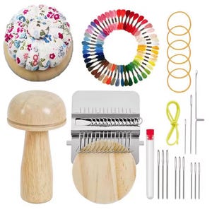 Puede incluir: Un conjunto de suministros de costura y manualidades, que incluye un alfiletero floral, un objeto de madera con forma de hongo, una disposición circular de hilos de bordar coloridos, agujas y una herramienta de tejido. También se incluyen gomas elásticas y un tubo pequeño.
