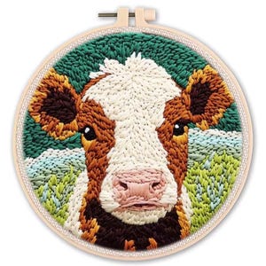 May include: A handcrafted embroidery hoop art piece featuring a detailed cow face. The cow has a white and brown face with a pink nose, set against a green and blue background. The embroidery is in a round wooden hoop.