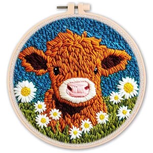 May include: Embroidered artwork featuring a brown cow with a pink nose and dark brown ears, surrounded by white daisies and green grass. The background is a textured blue. The artwork is set in a round wooden embroidery hoop.