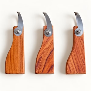 May include: Three identical woodworking tools featuring curved, sharpened metal blades attached to smooth, reddish-brown wooden handles. Each tool is secured with a silver-toned metal bolt and circular washer, showcasing a distinct wood grain pattern.