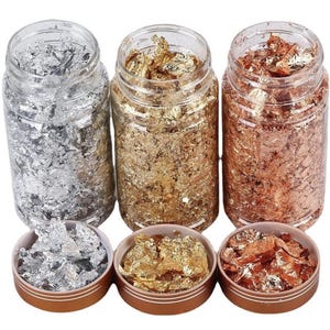 Può includere: Tre barattoli di plastica trasparente riempiti con scaglie metalliche color argento, oro e rame. Ogni barattolo è accompagnato da un coperchio circolare abbinato posto davanti, contenente una piccola porzione di scaglie argento, oro o rame.