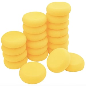 Puede incluir: Una colección de esponjas de espuma circulares de color amarillo brillante dispuestas en tres pilas verticales de alturas variables, con dos esponjas adicionales colocadas horizontalmente en primer plano, todas con textura porosa y lisa.