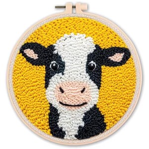 May include: A punch needle embroidery hoop featuring a smiling cow face. The cow has black and white markings, a pink nose, and black eyes. The background is yellow, and the hoop is made of wood.