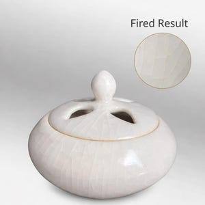 Może przedstawiać: Biały ceramiczny palnik do kadzidła z okrągłym korpusem i pokrywką z trzema okrągłymi otworami. Pokrywka ma mały, zaokrąglony uchwyt. Powierzchnia ma efekt spękanego szkliwa. Tekst "Fired Result" znajduje się w prawym górnym rogu.