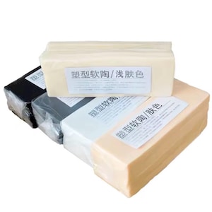 May include: A collection of rectangular blocks of polymer clay in various colors, including black, gray, white, and beige. Each block is wrapped in clear plastic and has a label with Chinese characters. The blocks are stacked on top of each other.