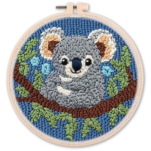 May include: A round embroidery hoop featuring a gray koala bear sitting on a brown branch, surrounded by green leaves and blue flowers. The background is a textured blue fabric. The koala has a white belly and tan ears.
