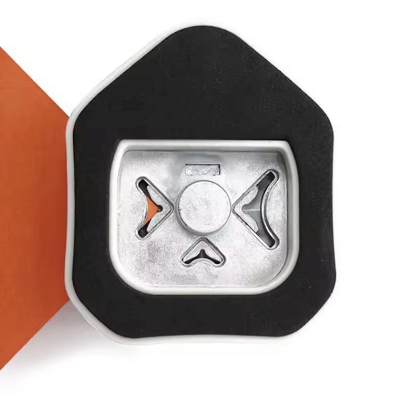 May include: Close-up of a silver-colored metal object with a black border. The object has a central circular element and three arrow-shaped cutouts. An orange corner is visible in the background.